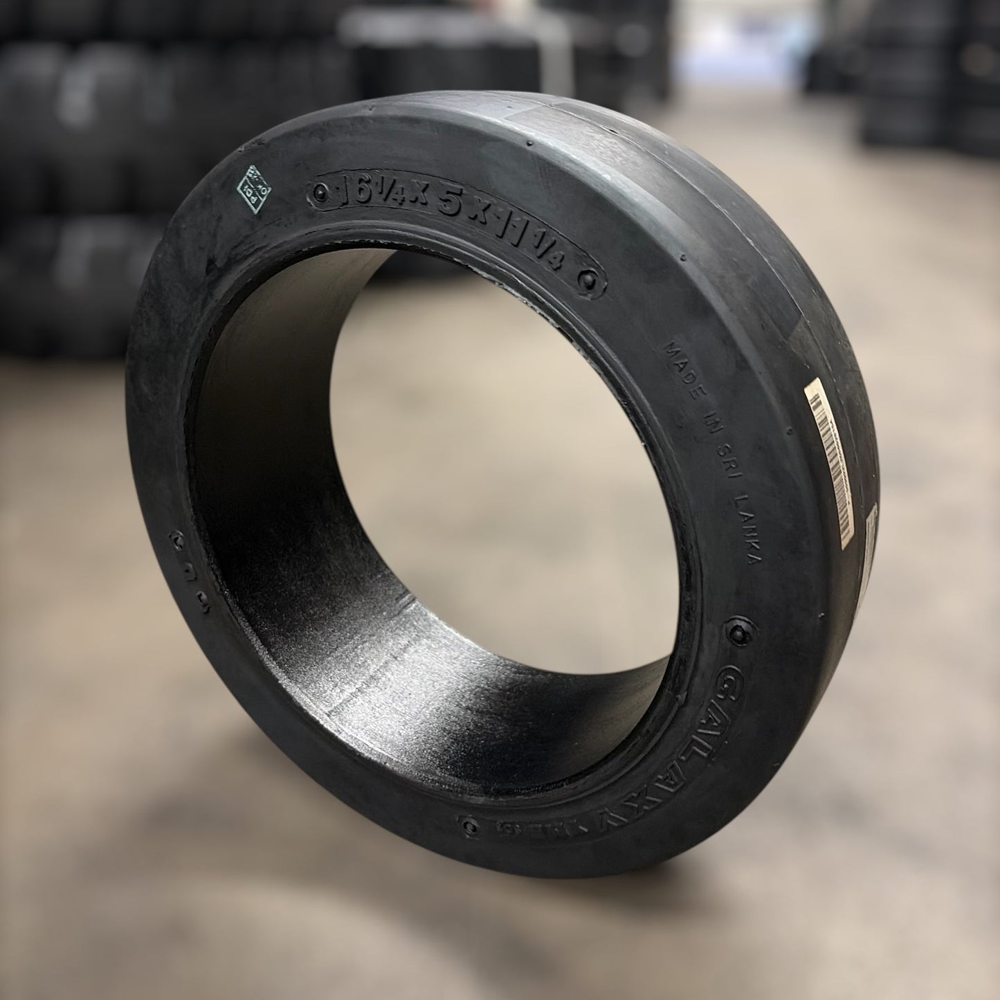 Black rubber bushing on a concrete floor with blurred tire stacks in the background