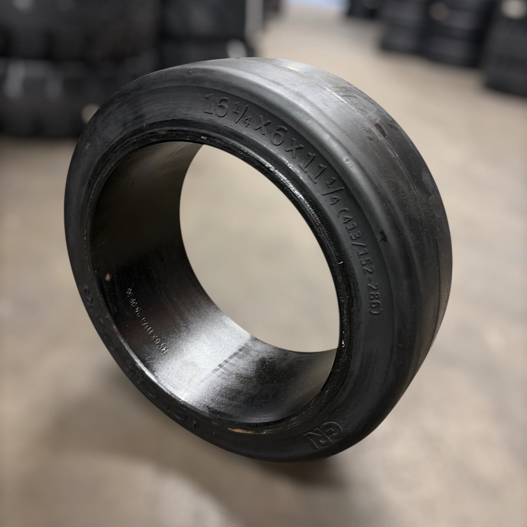 Black rubber forklift tire bushing on a concrete floor with tires in the background